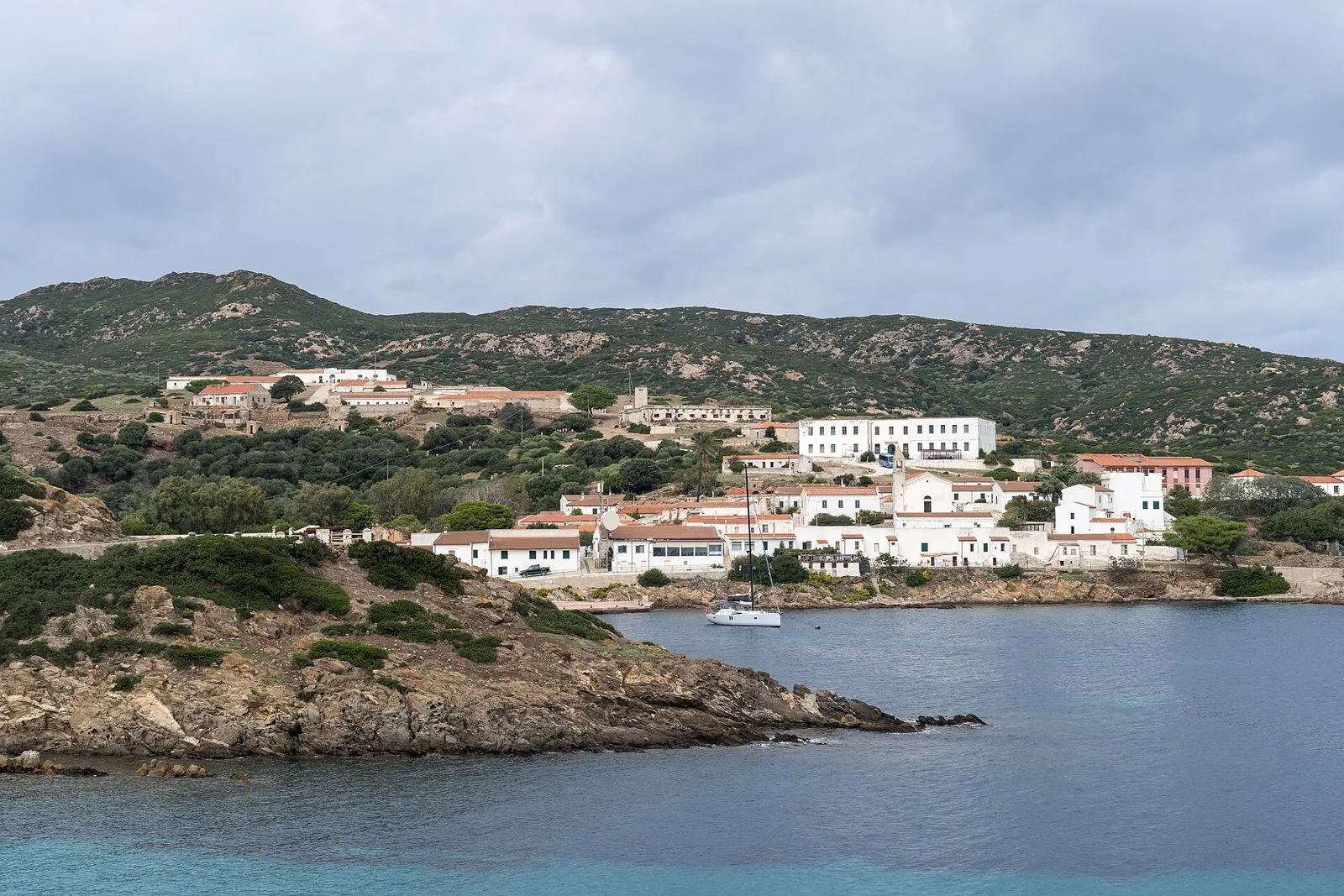 Il borgo di Cala d'Oliva sull'isola dell'Asinara, case bianche affacciate su una baia blu con colline di macchia alle spalle